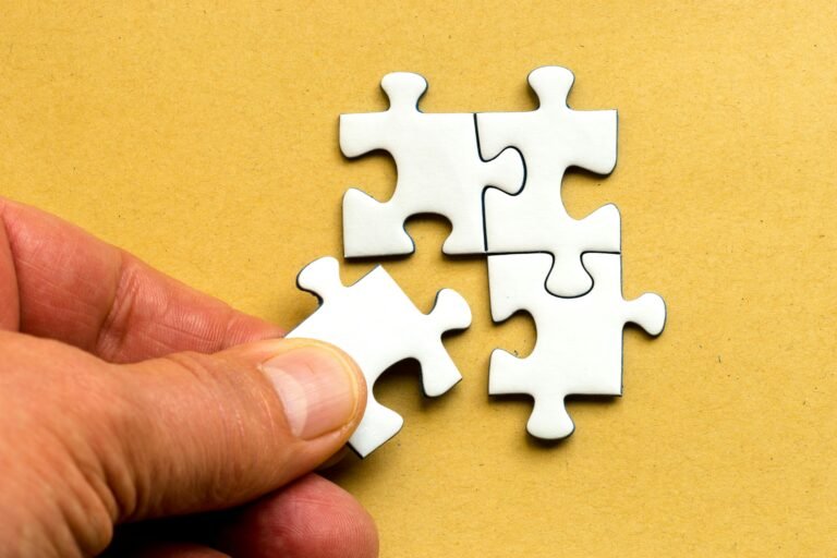 Close-up of a hand completing a white jigsaw puzzle on a yellow background.